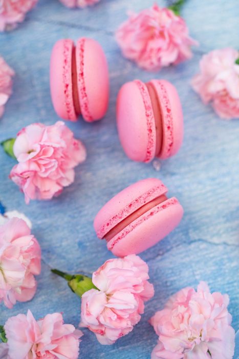 From above of tasty pink macaroons and aromatic carnations placed on blue table in daytime